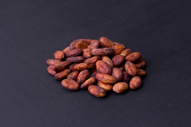 Soyulmamış çiğ kakao çekirdekleri siyah, modern beton arka planda yatıyor. Düz yat, maket yap, boşluğu kopyala. Kakao tozu, kakao içeceği ve çikolata yapmak için hammadde. Sağlık içeceği kavramı.