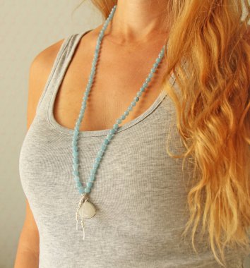 Doğal taşlardan alınan 108 boncuklu tespih gri gömlekli bir kıza takılıyor. Yazarın doğal taşlardan mücevherleri, Budizm, matra, dua, taşlardan tespih duası ve güzellik için..