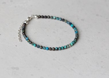 Chrysocolla bileziği. Elindeki bileklik doğal taştan yapılmış Chrysocolla. Doğal taşlardan yapılmış bilezik. Yazarın el yapımı mücevherleri. Hafif modern arkaplanda el yapımı bilezikler.