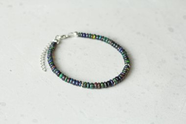 Siyah ateş opal el yapımı bileziği açık arkaplanda yatıyor. Doğal taşlardan yapılmış bilezik. Siyah ateş opalı. Doğal taşlardan yapılmış el yapımı mücevherler. Modern beton arka planda modern mücevherler.