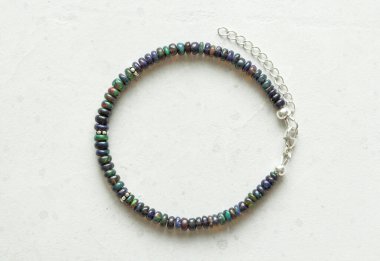 Siyah ateş opal el yapımı bileziği açık arkaplanda yatıyor. Doğal taşlardan yapılmış bilezik. Siyah ateş opalı. Doğal taşlardan yapılmış el yapımı mücevherler. Modern beton arka planda modern mücevherler.