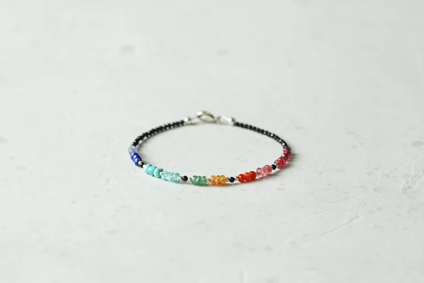 Bright multicolored bracelet. Ruby, coral, carnelian, citrine, emerald, apatite, amazonite, turquoise, lapis lazuli, tanzanite, black spinel. Handmade jewelry bracelets on light modern background.