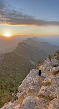 Genç şık kel erkek saksafoncu, güneşin ve güneşin arka planına karşı dağın tepesinde duruyor ve Kıbrıs 'ta altın saksafon çalıyor. Romantik müzisyen saksafoncu. Bulutların üstünde.