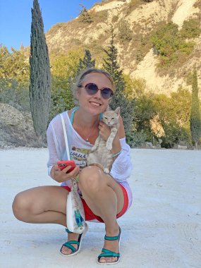 Genç bir Avrupalı kız, yaz aylarında, açık havada, kollarında güzel çizgili, açık bej bir sokak kedisi tutuyor. Kız gülümsüyor ve bir kediyi kollarında tutuyor. İnsanlar ve hayvanlar arasındaki gerçek dostluk..