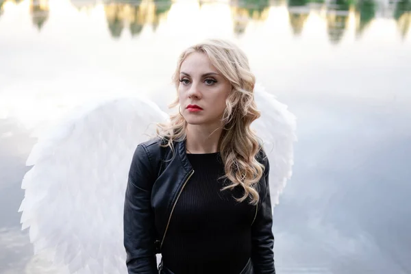 woman with white angel wings. wearing black leather clothes. fallen dark angel. demon. beast. girl in angel costume on halloween.