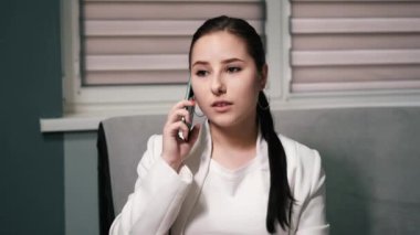 Üzgün, kızgın ve üzgün esmer iş kadını gri ofiste telefonla konuşuyor. Rahatsız edici, kötü bir telefon görüşmesi. Sorunlar, sorunlar. yavaş çekim