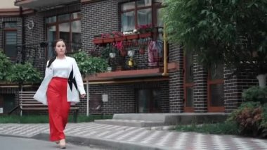 Kırmızı pantolonlu, beyaz bluzlu ve ceketli kendine güvenen esmer kadın sokakta yürüyor. yavaş çekim