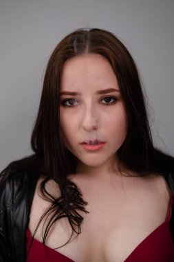 Siyah deri ceketli esmer kadın beyaz duman üflemiş. Gri arka planda sigara içen güzel bir kız. Kötü alışkanlık.