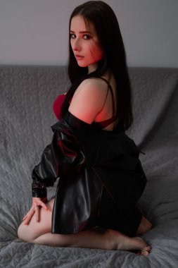 Kırmızı iç çamaşırlı ve deri ceketli seksi esmer. Karanlık odada kırmızı ışıkta poz veriyor..
