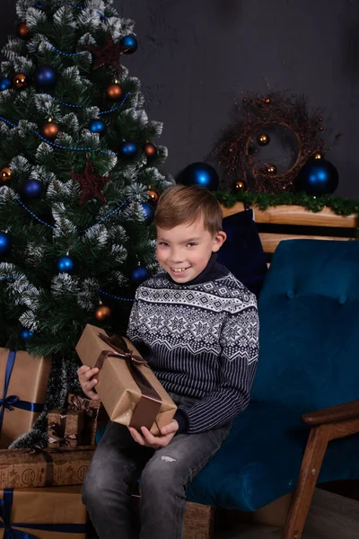 Щасливий красивий підліток блондинка в трикотажному светрі, що тримає різдвяний подарунок біля ялинки. святкування нового року . — стокове фото