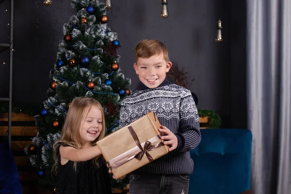 Szczęśliwe dzieci bawiące się prezentami świątecznymi. brat i siostra w pobliżu choinki daje sobie prezenty noworoczne. czas dla rodziny. rodzeństwo miłość. — Zdjęcie stockowe