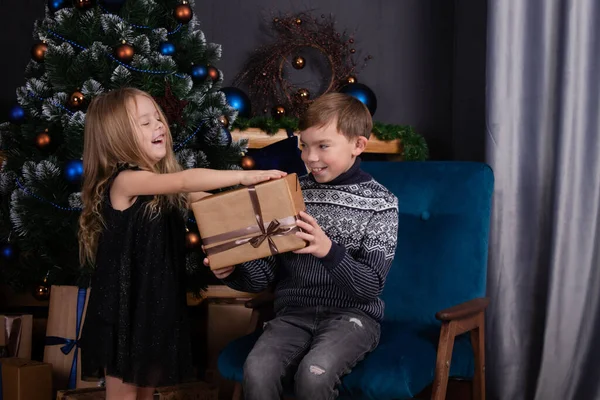 Счастливые дети играют с рождественскими подарками. Брат и сестра возле рождественской елки дарят друг другу новогодние подарки. семейное время. Братья и сестры любят. — стоковое фото