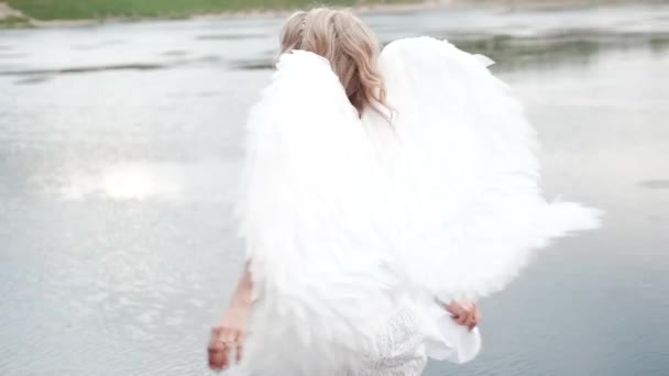 Vacker ängel i vit klänning. Fantastisk blond kvinna med långt lockigt hår och vita vingar. slow motion — Stockvideo