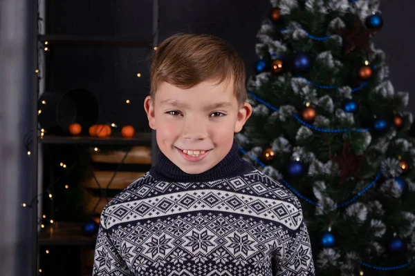 Okouzlující blondýnka dospívající chlapec v pletený tmavě modrý svetr v blízkosti zdobené vánoční stromeček. Veselé svátky. předvečer nových let — Stock fotografie