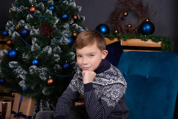 Süslü Noel ağacının yanında, koyu mavi süveterli yakışıklı sarışın çocuk. İyi tatiller. Yeni yıl arifesi — Stok fotoğraf