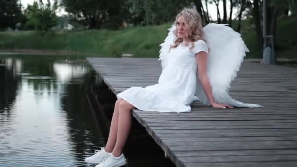 Charmante Blondine mit weißen Engelsflügeln, die am Wasser steht. schöne Frau im Engelskostüm. Göttin. Zeitlupe — Stockvideo