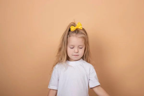 흰색 티셔츠를 입고 노란 활을 쓴 예쁜 금발의 여자 아이의 사진. ( 영어 ) 갈색 배경 — 스톡 사진