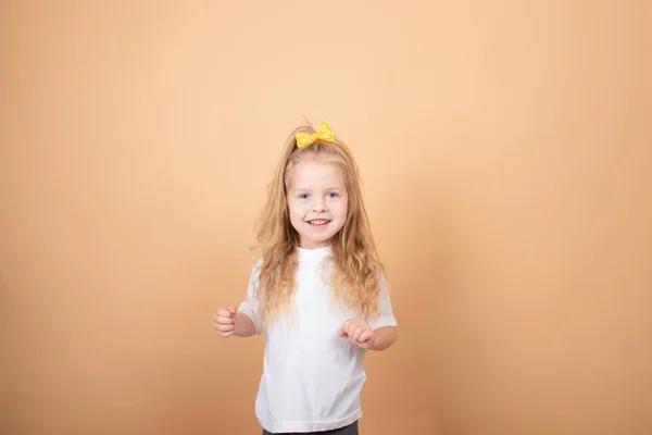 Portré egy édes szőke lányról fehér pólóban, sárga masnival a fején. barna alapon — Stock Fotó