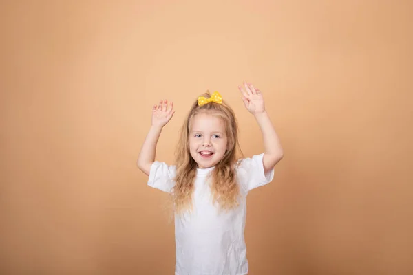Imádnivaló szőke lány fehér pólóban. barna - sárga háttér. ártatlanság gyermek portré — Stock Fotó