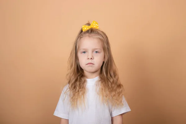 Retrato de uma menina loira doce em t-shirt branca e com arco amarelo na cabeça. sobre fundo marrom — Fotografia de Stock