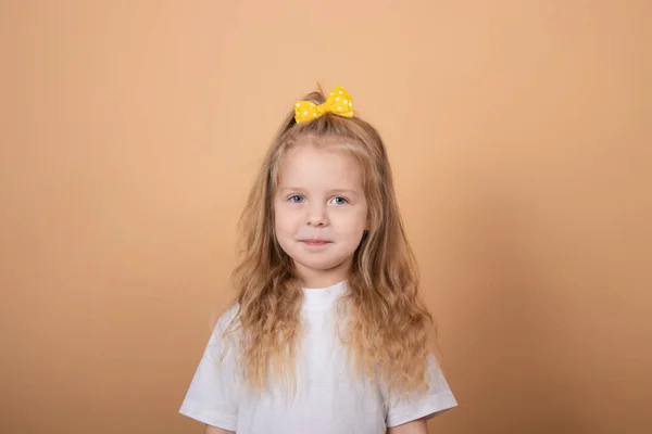 Imádnivaló szőke lány fehér pólóban. barna - sárga háttér. ártatlanság gyermek portré — Stock Fotó