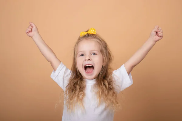 Retrato de uma menina loira doce em t-shirt branca e com arco amarelo na cabeça. sobre fundo marrom — Fotografia de Stock