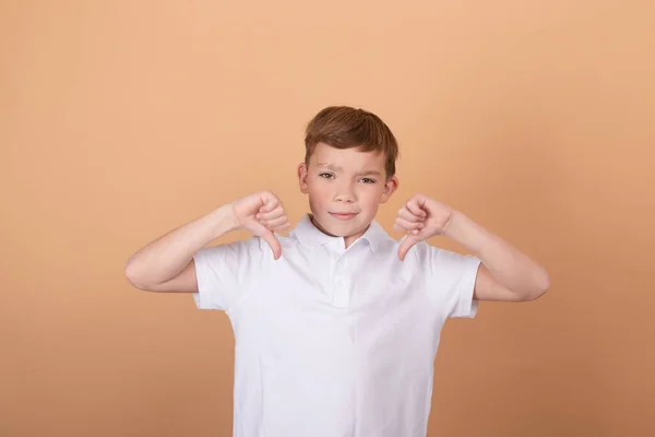 Krásný teenager chlapec na izolovaném hnědém pozadí ukazuje odpor - palec dolů gesto - s negativním výrazem a nesouhlas — Stock fotografie