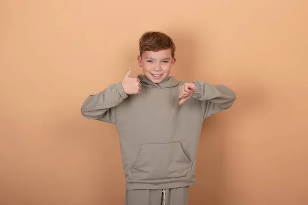 Teenage handsome boy against brown studio background showing thumbs up and thumbs down, difficult choice concept — Stock Photo, Image