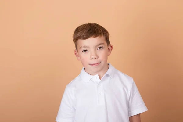 Érzelmi portré egy tinédzser fiúról. elbűvölő iskolás fiú. Gyönyörű gyerek. világosbarna háttér — Stock Fotó