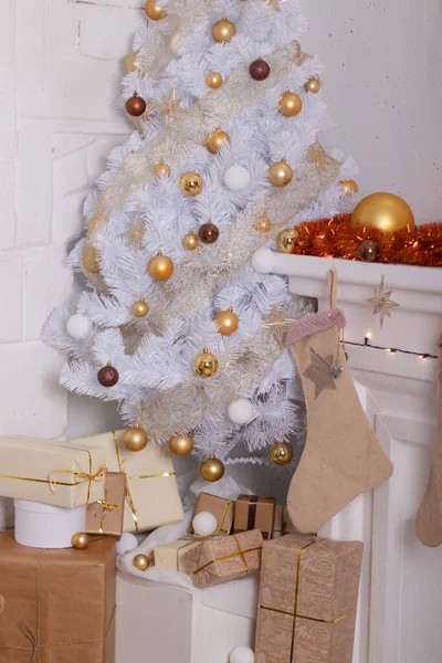 Nieuwjaarssfeer in de kamer. Ingerichte woonkamer met witte kerstboom. Feestelijke inrichting, bloemenslingers, geschenken. gouden kleuren tinten van de ruimte — Stockfoto