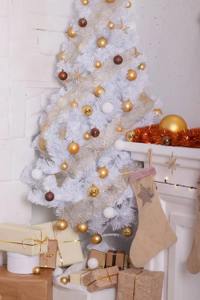 Nieuwjaarssfeer in de kamer. Ingerichte woonkamer met witte kerstboom. Feestelijke inrichting, bloemenslingers, geschenken. gouden kleuren tinten van de ruimte — Stockfoto