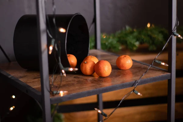 Chutné šťavnaté mandarinky v černé kulaté krabici na dřevěné polici. věnce na pozadí. s kopírovacím prostorem a mezerou pro text — Stock fotografie