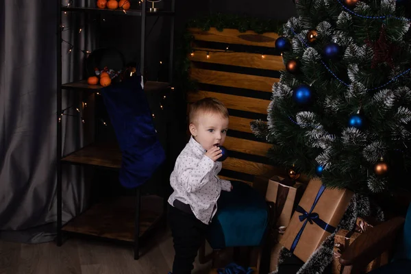 Little toddler blonde boy near christmas tree in dark loft room with blue decoration. happy new year — Zdjęcie stockowe