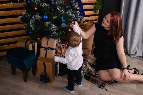 Little toddler boy with woman near christmas tree and decoration. son and mother on christmas eve. new year. single mother. incomplete family — Zdjęcie stockowe