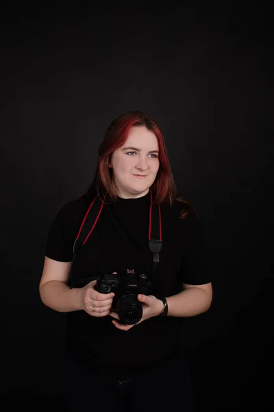 Redhead girl with a professional camera posing on black background. woman female photographer. — стоковое фото