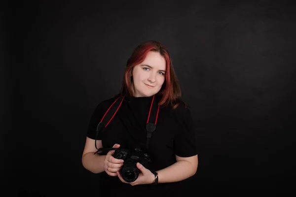 Redhead girl with a professional camera posing on black background. woman female photographer. — Stok fotoğraf