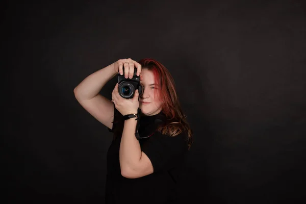 Redhead girl with a professional camera posing on black background. woman female photographer. — Stock Photo, Image