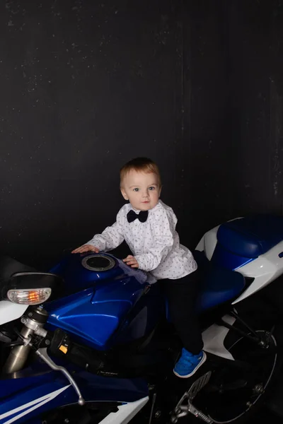 Pretty charming little boy on motorcycle on black background. little blonde child riding blue motor bike — Stock fotografie