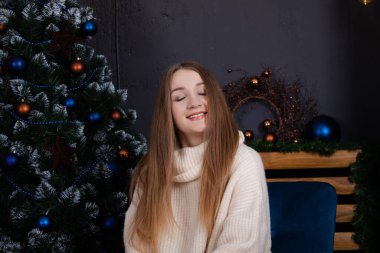 happy charming pretty woman in cosy beige knitted sweater near christmas tree. new year theme. Millennials
