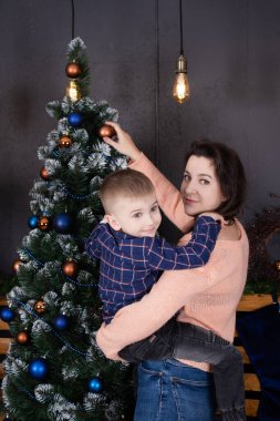 A mother helps a little boy decorate a Christmas tree in blue tones. Christmas holidays at home. Christmas tale.