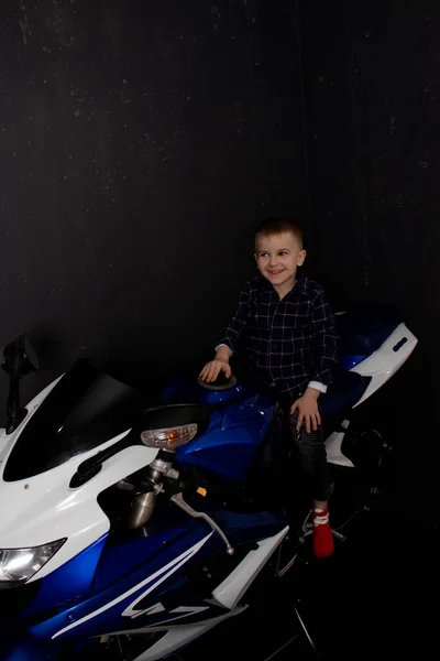 Pretty charming little boy on motorcycle on black background. little blonde child riding blue motor bike — Fotografia de Stock