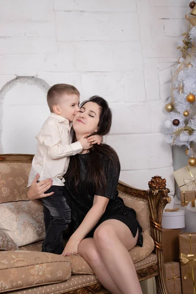 Атмосфера прийдешніх свят. портрет щасливої самотньої матері зі своїм маленьким приємним хлопчиком у білій світлій кімнаті біля ялинки в золотих тонах — стокове фото