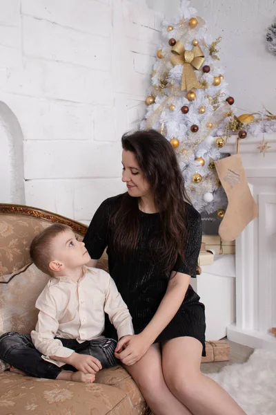 Атмосфера прийдешніх свят. портрет щасливої самотньої матері зі своїм маленьким приємним хлопчиком у білій світлій кімнаті біля ялинки в золотих тонах — стокове фото