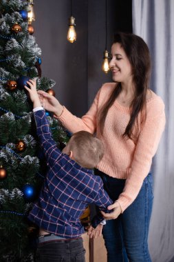 A mother helps a little boy decorate a Christmas tree in blue tones. Christmas holidays at home. Christmas tale.