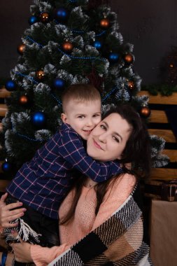 Young mother in a beige knitted sweater near a Christmas tree with her son. single mother with child. family time. mothers love