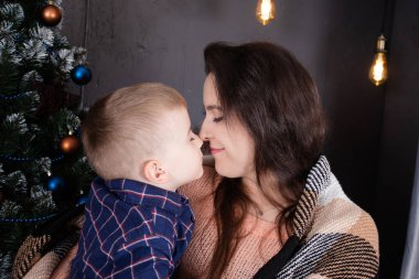 Young mother in a beige knitted sweater near a Christmas tree with her son. single mother with child. family time. mothers love