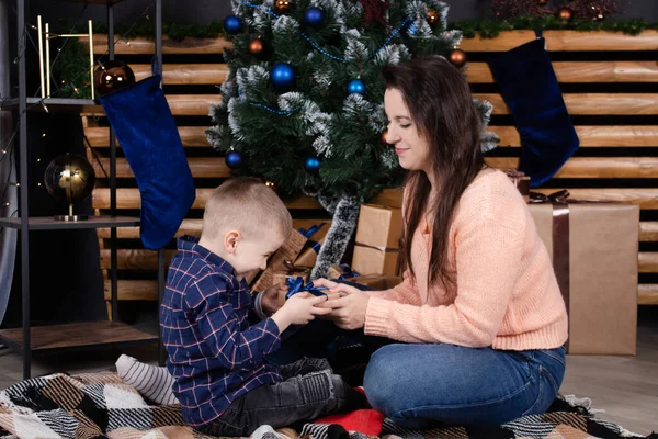 Merry Christmas and happy holidays. loving single mother with cheerful son play and cuddle near Christmas decoration, tree and gifts. Happy family, parent and child have fun on new year eve — Zdjęcie stockowe