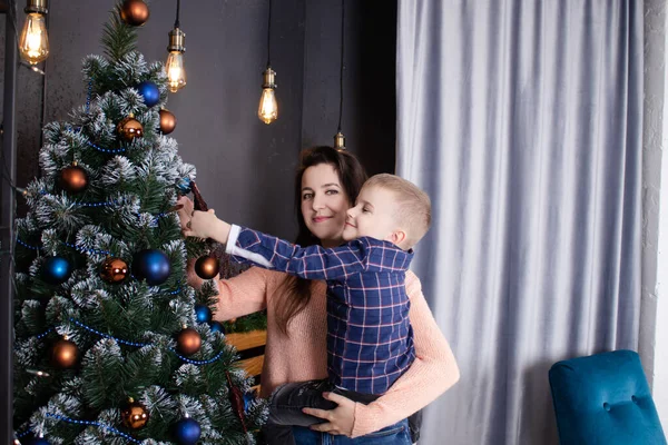 A mother helps a little boy decorate a Christmas tree in blue tones. Christmas holidays at home. Christmas tale. — Zdjęcie stockowe