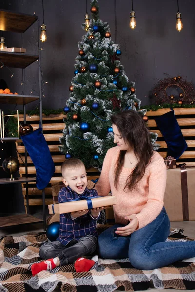 Merry Christmas and happy holidays. loving single mother with cheerful son play and cuddle near Christmas decoration, tree and gifts. Happy family, parent and child have fun on new year eve — Zdjęcie stockowe