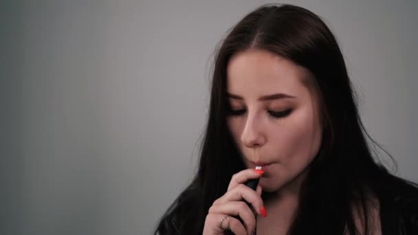 Mladá brunetka v černé kožené bundě vydechuje bílý kouř. krásná dívka milénium na šedém pozadí kouření. zlozvyk. Elektronická cigareta — Stock video